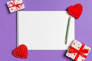 Blick von oben auf das Notizbuch, umgeben von Herzen und Geschenkboxen auf buntem Hintergrund. Valentinstag foto