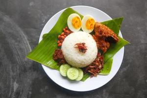 Nasi Lemak ist ein traditionelles malaiisches Gericht aus gekochten Eiern, Bohnen, Sardellen, Chilisauce und Gurken. aus einem Gericht, das auf einem Bananenblatt serviert wird foto