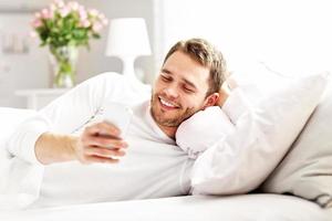 Schöner Mann, der mit Smartphone im Bett liegt foto