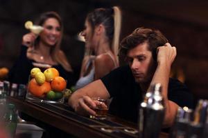 junger Mann sitzt allein in der Bar mit einem Glas Whiskey foto