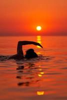 junge Frau, die bei Sonnenaufgang im Meer schwimmt foto