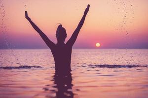 Silhouette einer jungen Frau, die bei Sonnenaufgang am Strand Yoga praktiziert foto