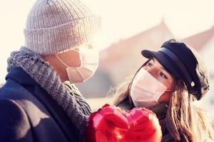 glückliches paar, das während der covid-19-pandemie den valentinstag in masken feiert foto