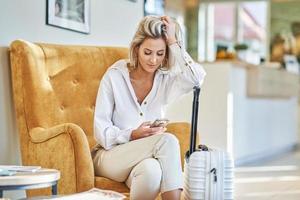 Geschäftsfrau mit Gepäck in moderner Hotellobby mit Smartphone foto