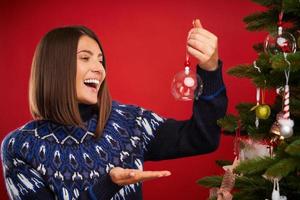 erwachsene Frau schmücken Weihnachtsbaum auf rotem Hintergrund foto