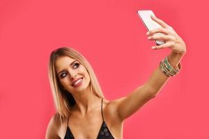 schöne erwachsene frau, die über rosa hintergrund mit smartphone aufwirft foto
