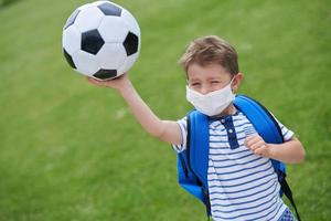Entzückender kleiner Junge mit Fußball und Schutzmaske auf dem Feld foto