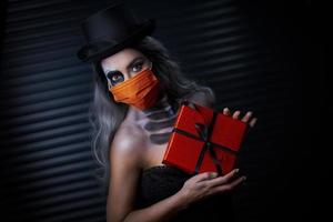 gruseliges Porträt einer Frau mit gotischem Make-up, die eine Maske trägt und ein Geschenk hält foto