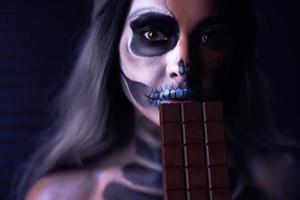 gruseliges porträt einer frau in halloween-gotischem make-up, das schokolade hält foto