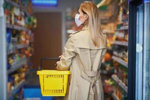 erwachsene Frau in medizinischer Maske, die Lebensmittel einkauft foto