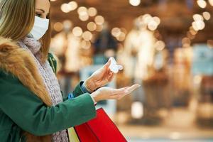 Mittelteil einer erwachsenen Frau im Einkaufszentrum, die eine Maske trägt und Händedesinfektionsmittel verwendet foto