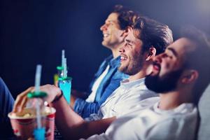 gruppe glücklicher freunde, die im kino sitzen, film ansehen und popcorn essen foto