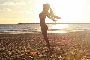 junge Frau der Silhouette, die Yoga am Strand bei Sonnenuntergang praktiziert foto