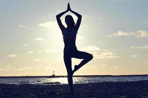 junge Frau der Silhouette, die Yoga am Strand bei Sonnenuntergang praktiziert foto