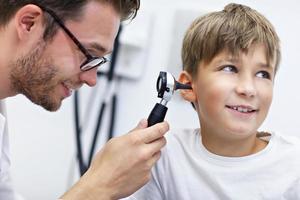 Nahaufnahme eines männlichen Arztes, der das Ohr des Jungen mit einem Otoskop untersucht foto