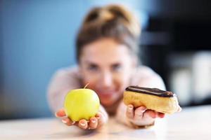 Frau, die zwischen Apfel und Eclair wählt foto