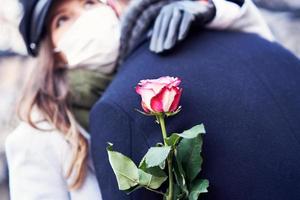 glückliches paar, das während der covid-19-pandemie den valentinstag in masken feiert foto