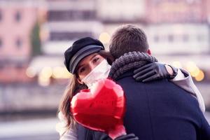 glückliches paar, das während der covid-19-pandemie den valentinstag in masken feiert foto