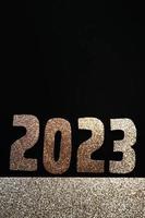 frohes neues jahr 2023. goldene zahlen auf schwarzem hintergrund mit glitzer foto