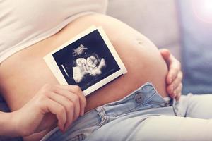 Nahaufnahme der schwangeren Frau, die Ultraschall auf ihrem Bauch hält foto
