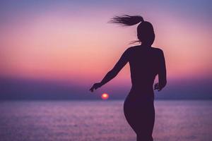 Silhouette einer sexy Frau, die bei Sonnenaufgang am Strand posiert foto