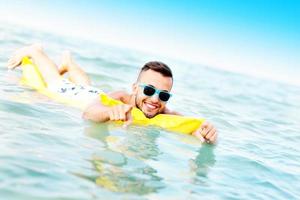 junger Mann, der auf einer Matratze schwimmt foto