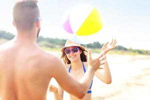 junges Paar spielt mit einem Ball am Strand foto