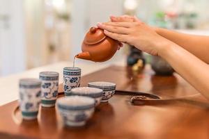 tee wird in die tasse nahaufnahme gegossen. asiatischer tee auf hölzernem bambustisch, chinesischer tee wird von hand sanft gegossen foto