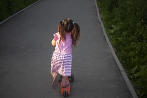 Kind auf Roller. Mädchen reitet die Straße hinunter. Details zum Spaziergang mit Kind. foto
