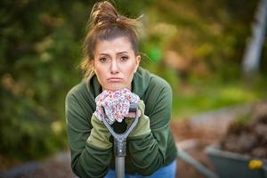 Bild einer müden Frau, die mit Werkzeugen im Garten arbeitet foto