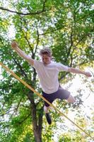 junger Mann balanciert und springt auf Slackline. Mann geht, springt und balanciert auf einem Seil im Park. foto
