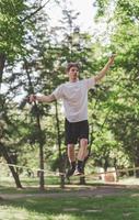 junger Mann balanciert und springt auf Slackline. Mann geht, springt und balanciert auf einem Seil im Park. foto