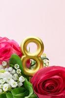 Rosenstrauß mit Maiglöckchen und goldener Zahl acht 8 auf rosa Hintergrund. vertikal. feiertag, 8. märz, internationaler frauentag. Platz kopieren foto