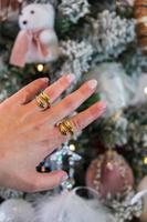 Mädchenhand, die goldene Ringe mit einem Weihnachtsbaum im Hintergrund trägt. festliche weihnachts- und geschenkkonzepte. foto