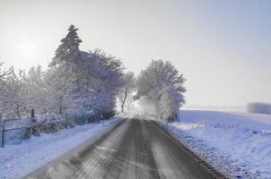 Blick auf eine schneebedeckte Landstraße im Winter mit Sonnenschein und blauem Himmel. foto