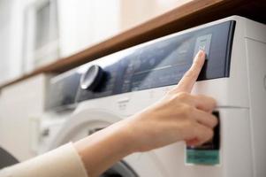 Nahaufnahme einer Frau, die mit der Hand die Tasten der Waschmaschine drückt, um das Programm einzustellen oder die Wäsche zu starten, Lifestyle-Konzept für die Gesundheitsfürsorge foto
