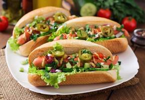 Hot Dog mit Jalapenopfeffer, Tomaten, Gurken und Salat auf Holzhintergrund foto