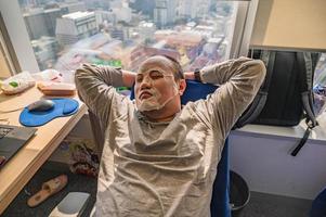 asiatischer dicker mann, der in seinem büro mit sonnenlicht und stadtbild eine gesichtsmaske für die schönheit macht foto