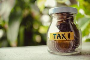 das Glas voll mit den Münzen. Steuerwort auf dem Glas. Finanz- und Steuerkonzept. thailändisches Badegeld in einem Glas. foto