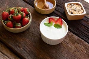 Erdbeerjoghurt in einer Holzschale mit Müsli, Honig, Minze und frischen Erdbeeren auf Holzhintergrund. Konzept für gesunde Ernährung. foto