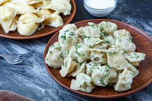 traditionelle russische pelmeni oder ravioli, knödel mit fleisch auf holzschwarzem hintergrund. russisches essen und russisches küchenkonzept. foto