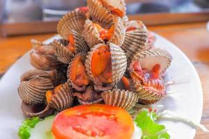 gedünstete Herzmuscheln Gekochte Herzmuscheln werden auf einen weißen Teller gelegt. garniert mit in Scheiben geschnittenen Tomaten. foto