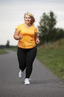 übergewichtige europäerin mittleren alters im trainingsanzug joggen, sport treiben. foto