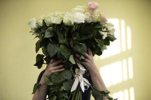 frau, die einen riesigen blumenstrauß aus weißen rosen hält, die ihr gesicht bedecken foto