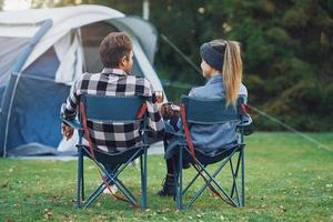 junges nettes paar sitzt auf stühlen vor dem zelt beim camping foto