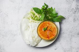 Curry-Küche asiatisches Essen auf dem Tisch - thailändische Curry-Suppenschüssel mit thailändischen Reisnudeln Fadennudeln Zutat Kräutergemüse auf weißem Teller foto