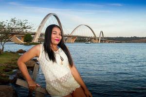 Schöne junge Brasilianerin mit einem schönen Lächeln im Park mit der JK-Brücke in Brasilien, im Hintergrund foto
