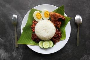 Nasi Lemak ist ein traditionelles malaiisches Gericht aus gekochten Eiern, Bohnen, Sardellen, Chilisauce und Gurken. aus einem Gericht, das auf einem Bananenblatt serviert wird foto