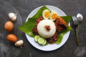 Nasi Lemak ist ein traditionelles malaiisches Gericht aus gekochten Eiern, Bohnen, Sardellen, Chilisauce und Gurken. aus einem Gericht, das auf einem Bananenblatt serviert wird foto