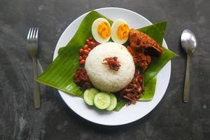 Nasi Lemak ist ein traditionelles malaiisches Gericht aus gekochten Eiern, Bohnen, Sardellen, Chilisauce und Gurken. aus einem Gericht, das auf einem Bananenblatt serviert wird foto